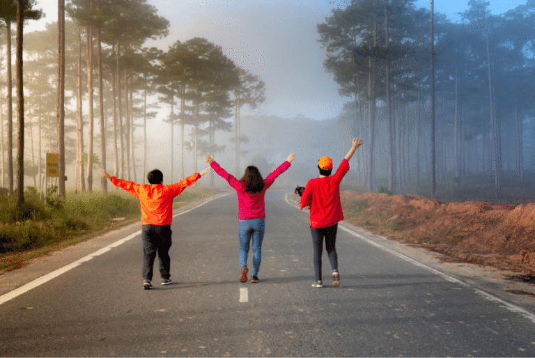Three people walking down a forest road with arms raised in joy, symbolising freedom and recovery.
